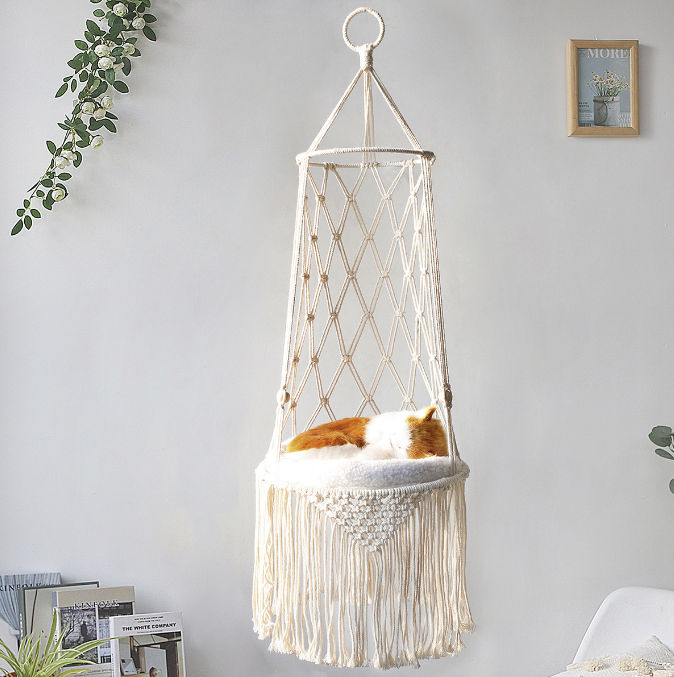 Hamac suspendu en macramé avec coussin moelleux et chat endormi, accroché au mur d’un salon.