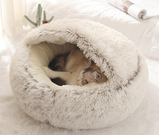 Chat endormi dans un lit à capuche moelleux en fausse fourrure grise, intérieur beige chaud.